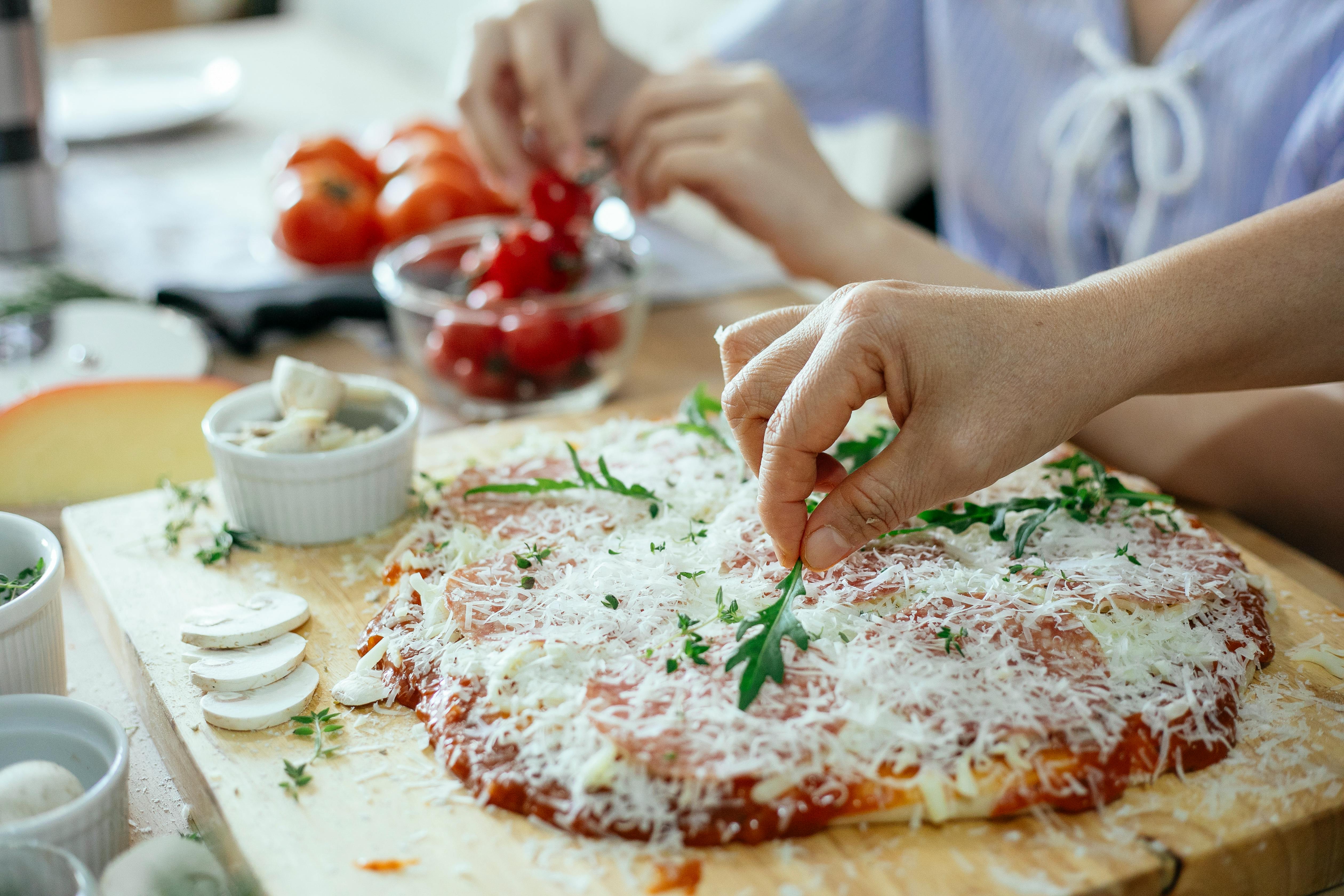 Grated cheese and rocket being added to a flatbread on a wooden board